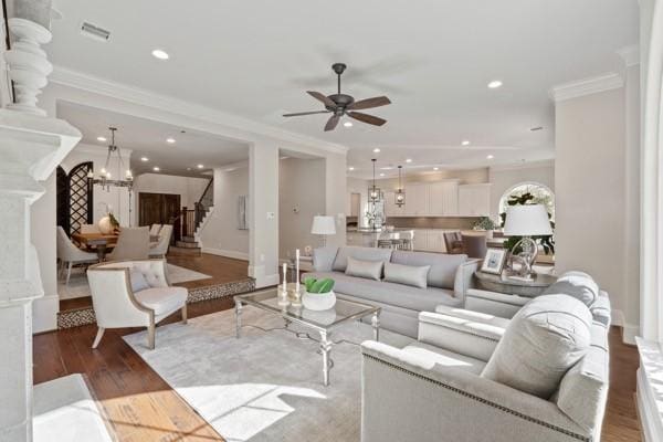 living room with hardwood / wood-style flooring, ceiling fan with notable chandelier, and crown molding