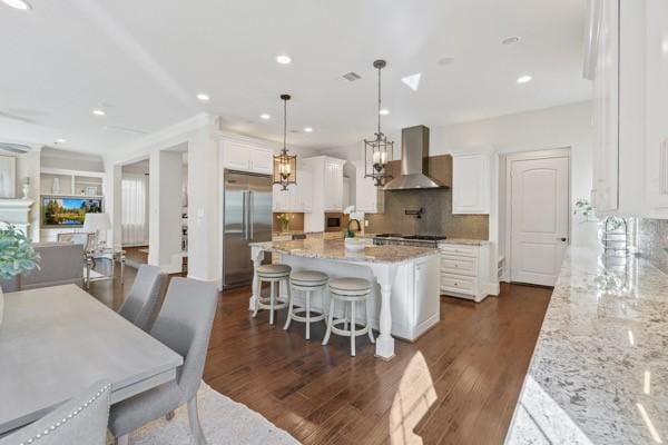 kitchen with pendant lighting, a center island, white cabinets, wall chimney exhaust hood, and stainless steel built in refrigerator