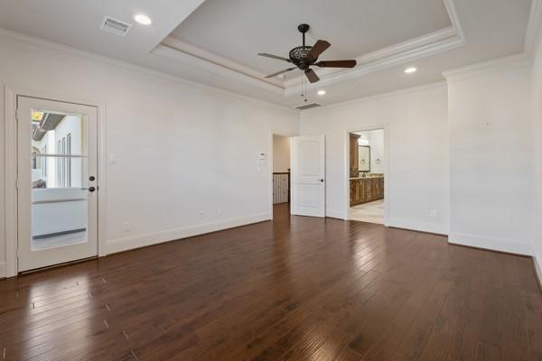 empty room featuring dark wood-type flooring, a tray ceiling, ceiling fan, and ornamental molding