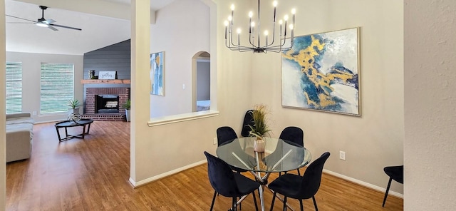 dining room with ceiling fan with notable chandelier, hardwood / wood-style flooring, a brick fireplace, and lofted ceiling