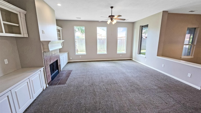 unfurnished living room featuring a fireplace, dark colored carpet, and ceiling fan