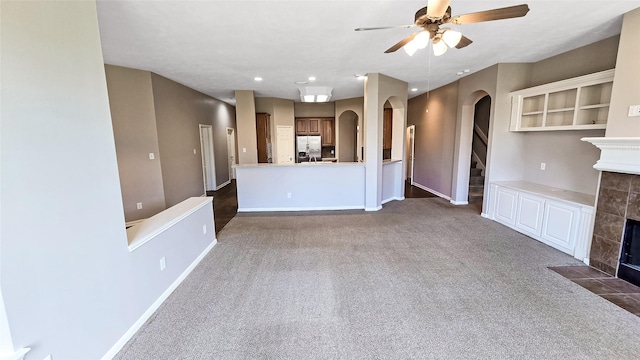 unfurnished living room featuring ceiling fan, a fireplace, and dark carpet