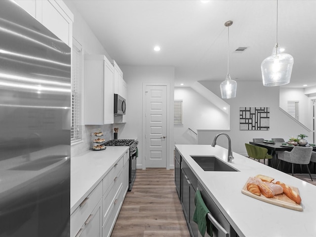 kitchen featuring stainless steel appliances, sink, pendant lighting, light hardwood / wood-style flooring, and white cabinets