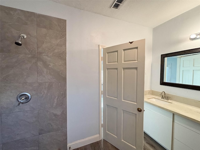 bathroom with hardwood / wood-style flooring, vanity, tiled shower, and a textured ceiling