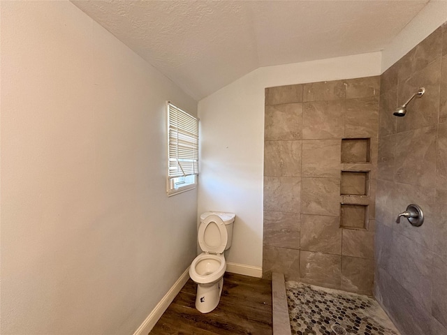 bathroom with a textured ceiling, tiled shower, hardwood / wood-style floors, toilet, and lofted ceiling