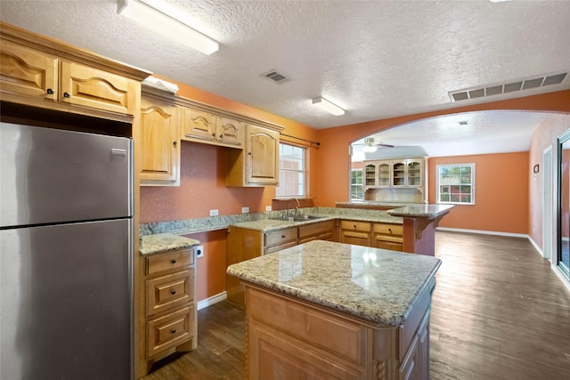 kitchen featuring stainless steel refrigerator, kitchen peninsula, a center island, and dark hardwood / wood-style floors