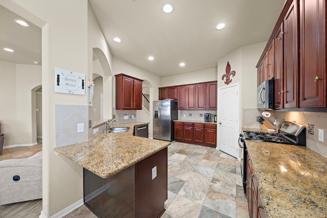 kitchen with appliances with stainless steel finishes, sink, a kitchen bar, light stone counters, and kitchen peninsula