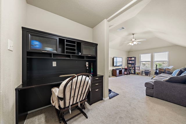 carpeted home office with vaulted ceiling, built in desk, ceiling fan, and a textured ceiling