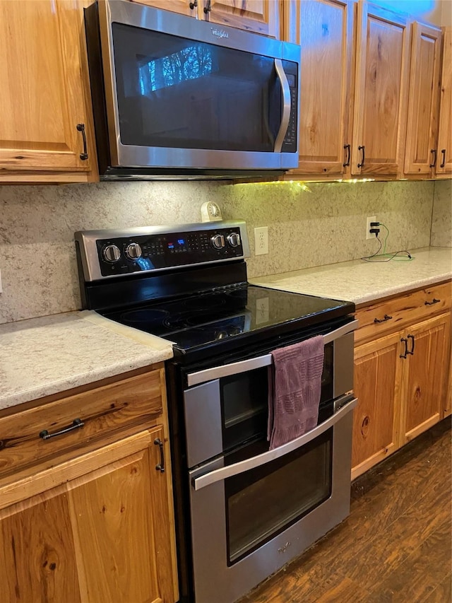 kitchen with backsplash, stainless steel appliances, light stone counters, and dark hardwood / wood-style floors