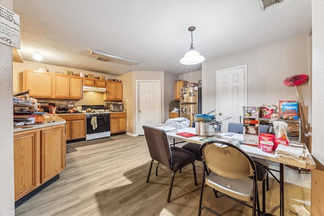 kitchen featuring white gas stove, stainless steel fridge, hanging light fixtures, and light hardwood / wood-style flooring