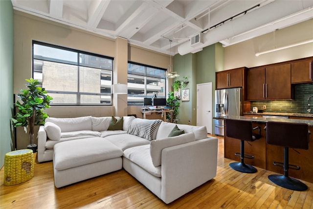 living room with light wood-type flooring, beamed ceiling, and a high ceiling