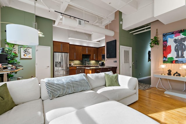 living room featuring sink, light hardwood / wood-style flooring, and a towering ceiling