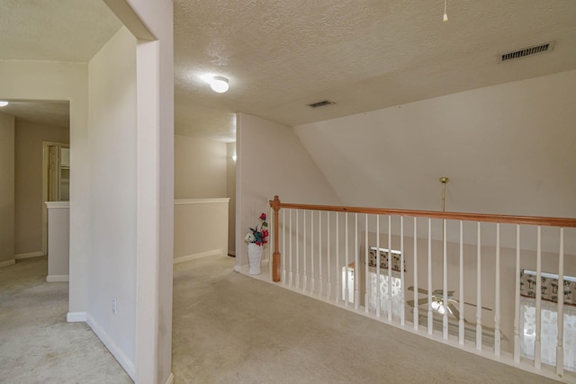 corridor featuring a textured ceiling, light carpet, and vaulted ceiling