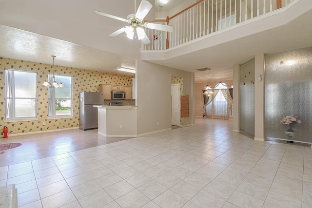 unfurnished living room featuring a towering ceiling, light tile patterned floors, ceiling fan with notable chandelier, and a wealth of natural light