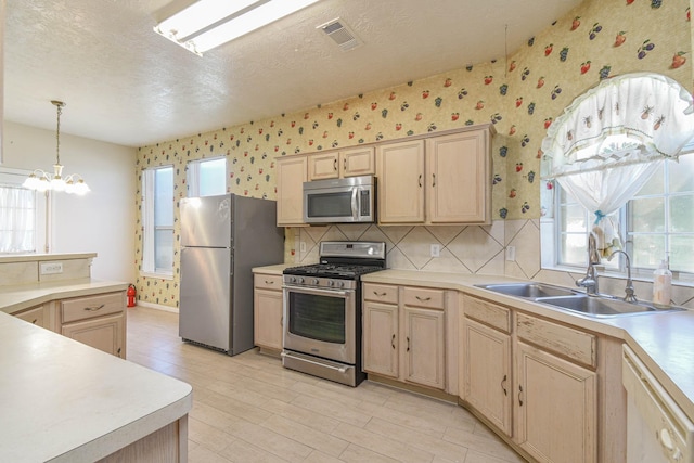 kitchen with light brown cabinets, sink, stainless steel appliances, and an inviting chandelier