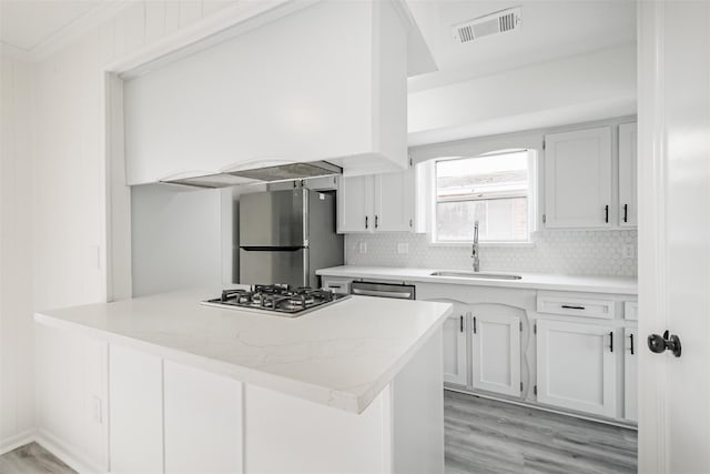 kitchen with sink, white cabinetry, appliances with stainless steel finishes, kitchen peninsula, and backsplash