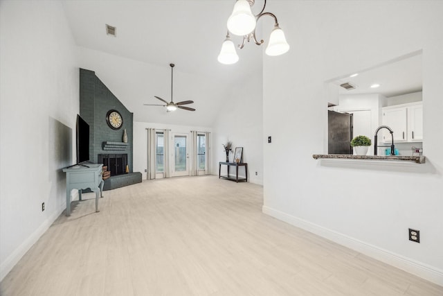 living room with ceiling fan with notable chandelier, high vaulted ceiling, a brick fireplace, and light hardwood / wood-style floors