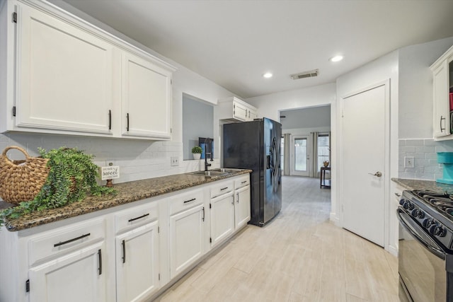 kitchen featuring decorative backsplash, light wood-type flooring, black appliances, dark stone countertops, and white cabinetry