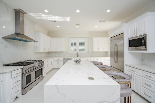 kitchen featuring a breakfast bar, built in appliances, white cabinets, a kitchen island, and wall chimney exhaust hood