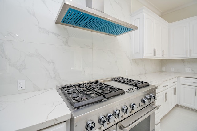 kitchen featuring tasteful backsplash, white cabinets, stainless steel stove, and wall chimney range hood