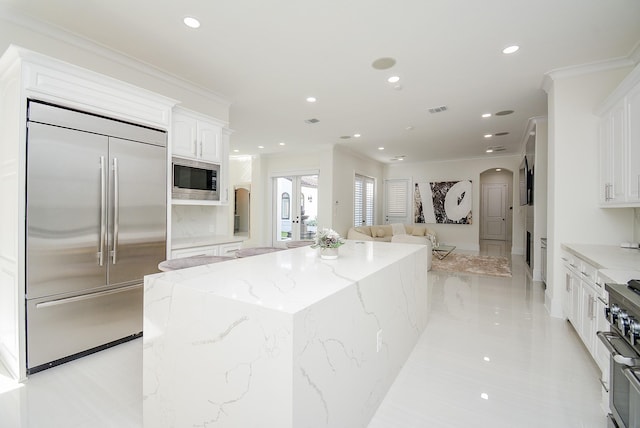 kitchen featuring white cabinetry, a center island, built in appliances, light stone counters, and ornamental molding