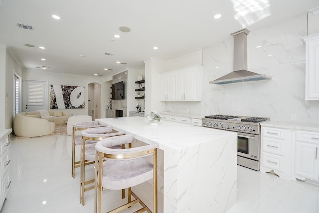 kitchen with stainless steel stove, a kitchen bar, white cabinets, a kitchen island, and wall chimney exhaust hood