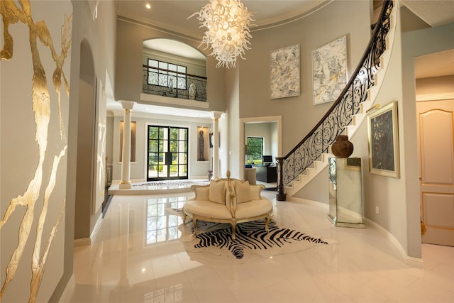 tiled entrance foyer featuring a high ceiling, decorative columns, ornamental molding, and a notable chandelier