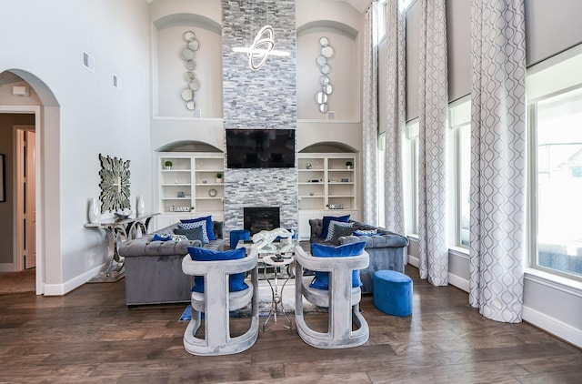 living room with built in shelves, dark hardwood / wood-style floors, a stone fireplace, and a towering ceiling