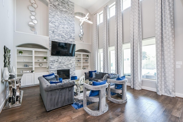 living room featuring dark hardwood / wood-style floors, a healthy amount of sunlight, a stone fireplace, and a high ceiling