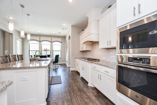 kitchen featuring appliances with stainless steel finishes, light stone counters, pendant lighting, white cabinetry, and an island with sink