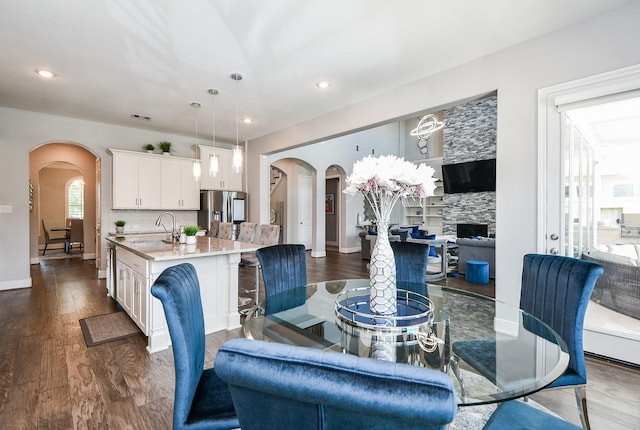 dining room featuring a stone fireplace, sink, and dark wood-type flooring