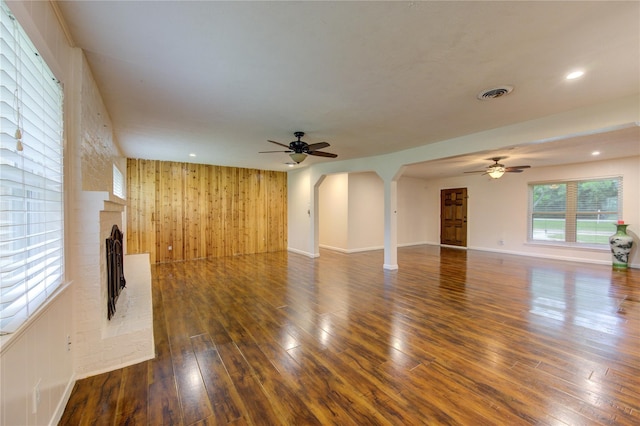 unfurnished living room featuring a fireplace, wood walls, dark hardwood / wood-style flooring, and ceiling fan