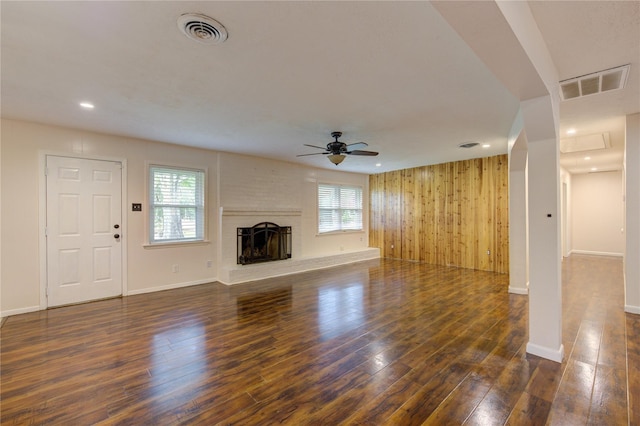 unfurnished living room featuring ceiling fan, a fireplace, dark wood-type flooring, and wood walls