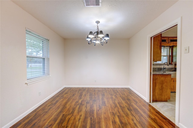 spare room featuring dark hardwood / wood-style floors, sink, a textured ceiling, and an inviting chandelier