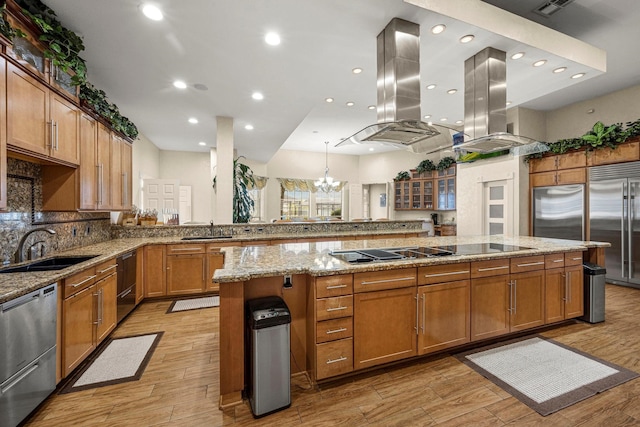 kitchen with island range hood, sink, light stone counters, and appliances with stainless steel finishes