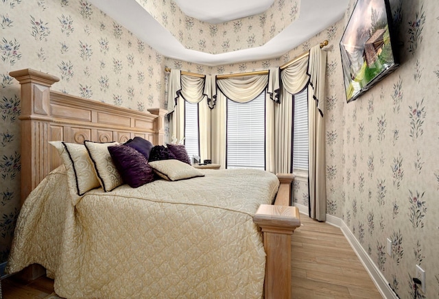 bedroom with light wood-type flooring and a tray ceiling