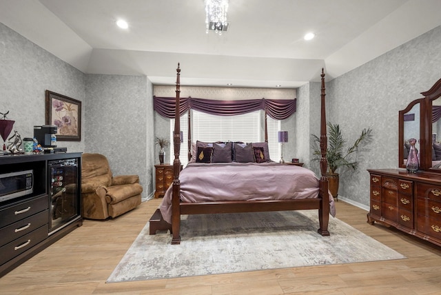 bedroom with an inviting chandelier, beverage cooler, vaulted ceiling, and light wood-type flooring