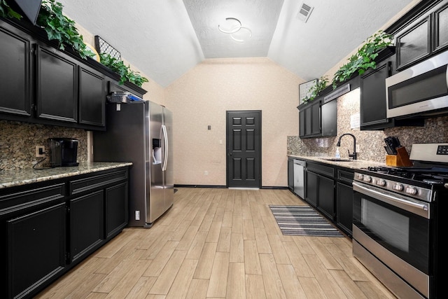 kitchen with sink, vaulted ceiling, light stone countertops, tasteful backsplash, and stainless steel appliances