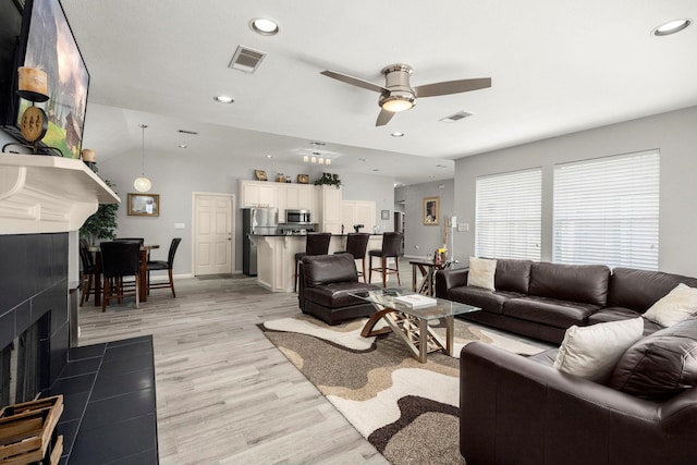 living room with a fireplace, light wood-type flooring, and ceiling fan