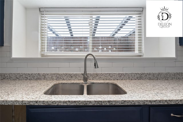 interior details featuring decorative backsplash, sink, and light stone counters