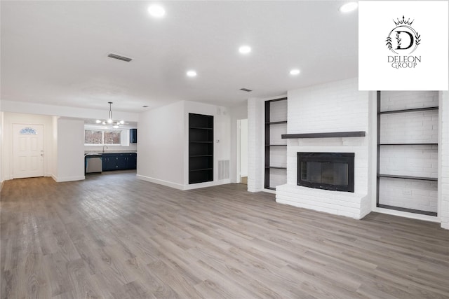 unfurnished living room with a notable chandelier, sink, wood-type flooring, and a fireplace