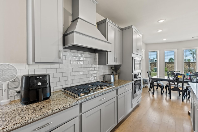 kitchen featuring backsplash, gray cabinets, premium range hood, and stainless steel appliances