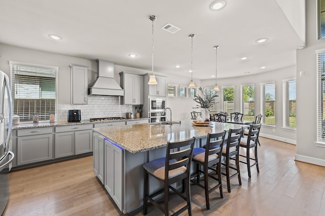 kitchen featuring pendant lighting, a breakfast bar, premium range hood, built in microwave, and a large island