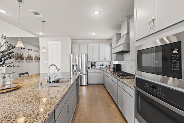 kitchen with backsplash, premium range hood, hanging light fixtures, sink, and appliances with stainless steel finishes