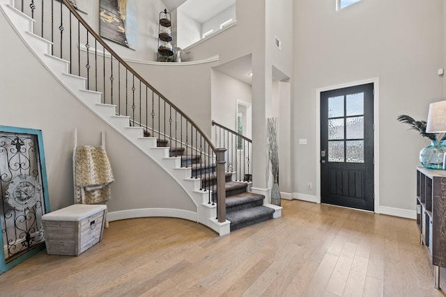 entryway with a towering ceiling, a healthy amount of sunlight, and light wood-type flooring