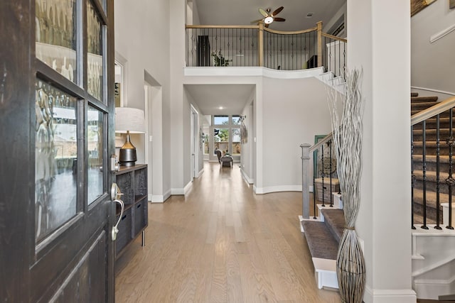 foyer entrance with a towering ceiling, light hardwood / wood-style floors, and ceiling fan