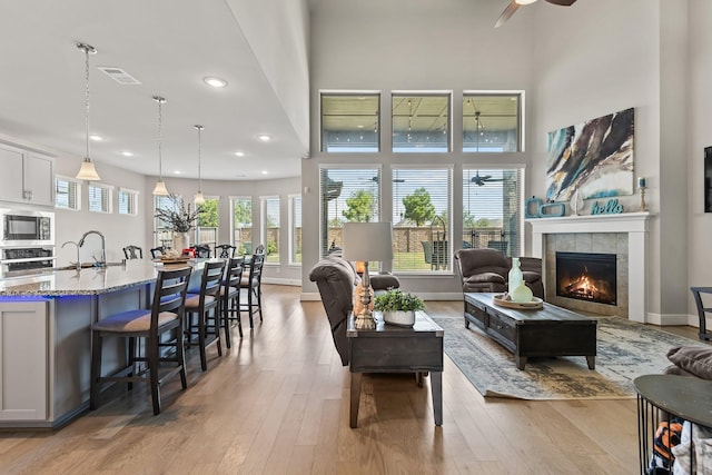 living room with a high ceiling, a tile fireplace, sink, ceiling fan, and light wood-type flooring