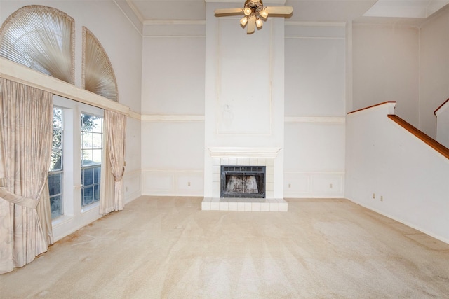 unfurnished living room with ceiling fan, a high ceiling, crown molding, light carpet, and a fireplace