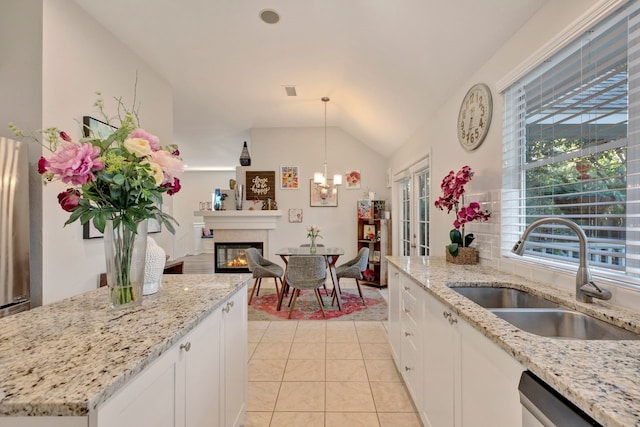 kitchen featuring vaulted ceiling, sink, light tile patterned floors, white cabinets, and hanging light fixtures