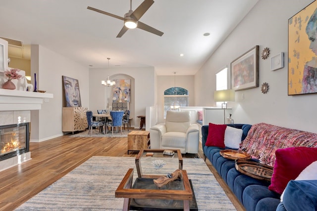 living room featuring a tile fireplace, ceiling fan with notable chandelier, and hardwood / wood-style flooring